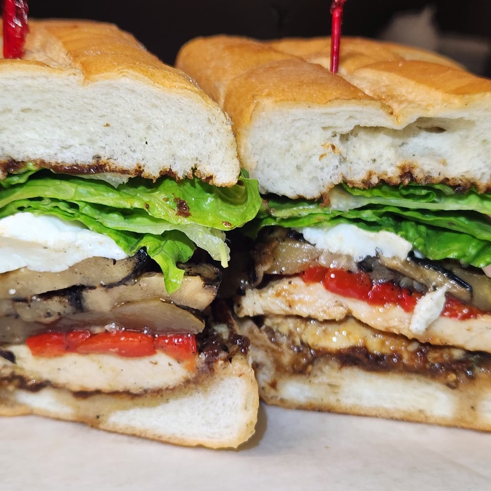 Close-up of a sliced Nostra Pizza sandwich with chicken, red peppers, mushrooms, lettuce, and cheese.