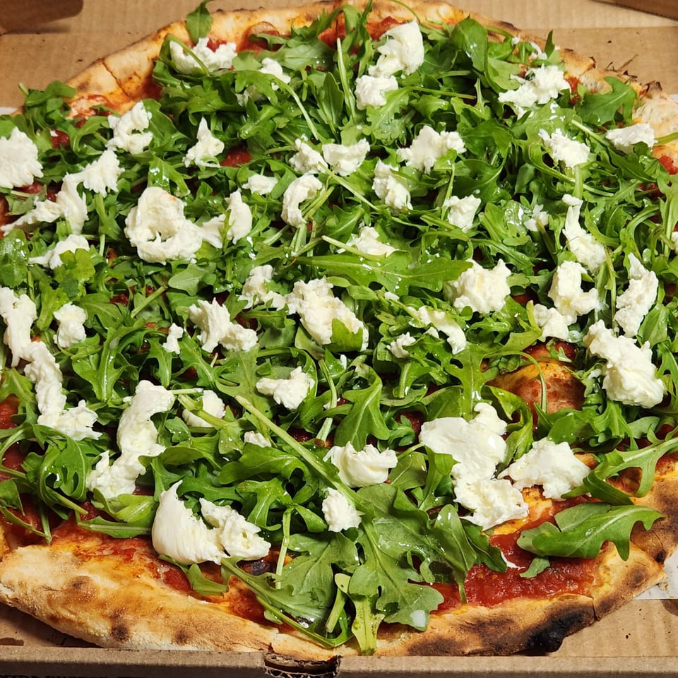 Nostra Pizza Voorhees' pizza with fresh arugula and dollops of ricotta cheese in a cardboard box.