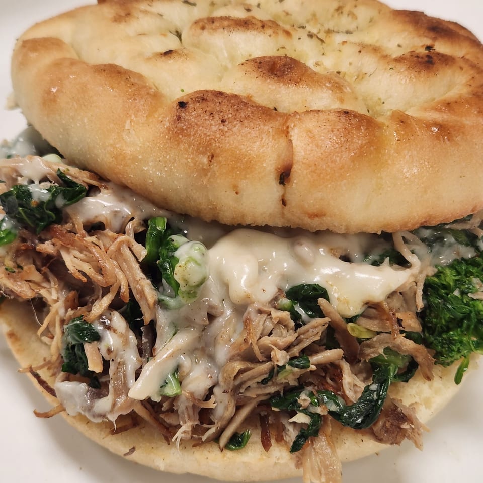 A Nostra Pizza Voorhees sandwich with shredded meat, greens, and melted cheese on focaccia bread.
