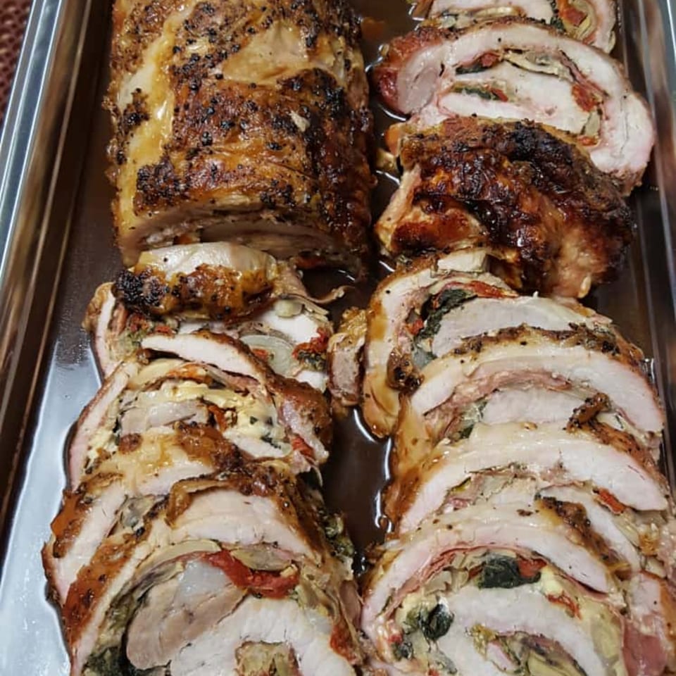 Two large, sliced roasted pork roasts with savory stuffing, in a metal pan with juices.
