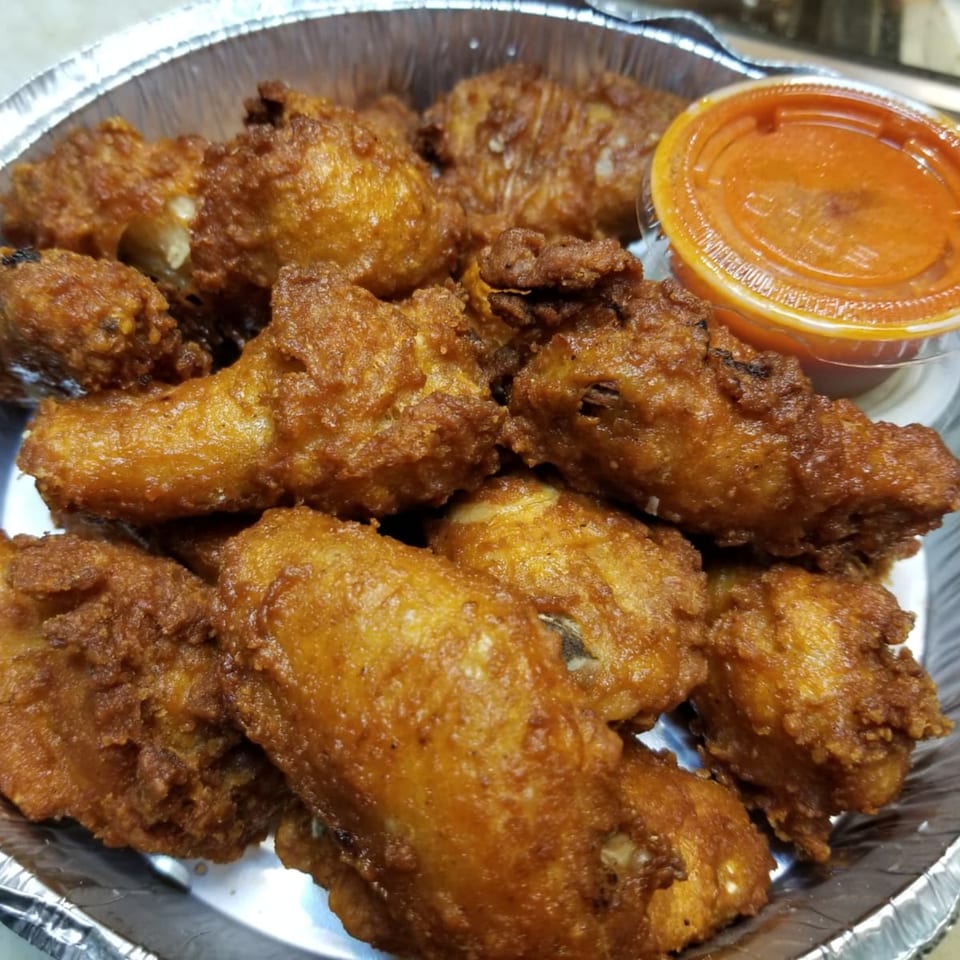 Crispy golden-brown chicken wings in a foil container with a side of orange dipping sauce.